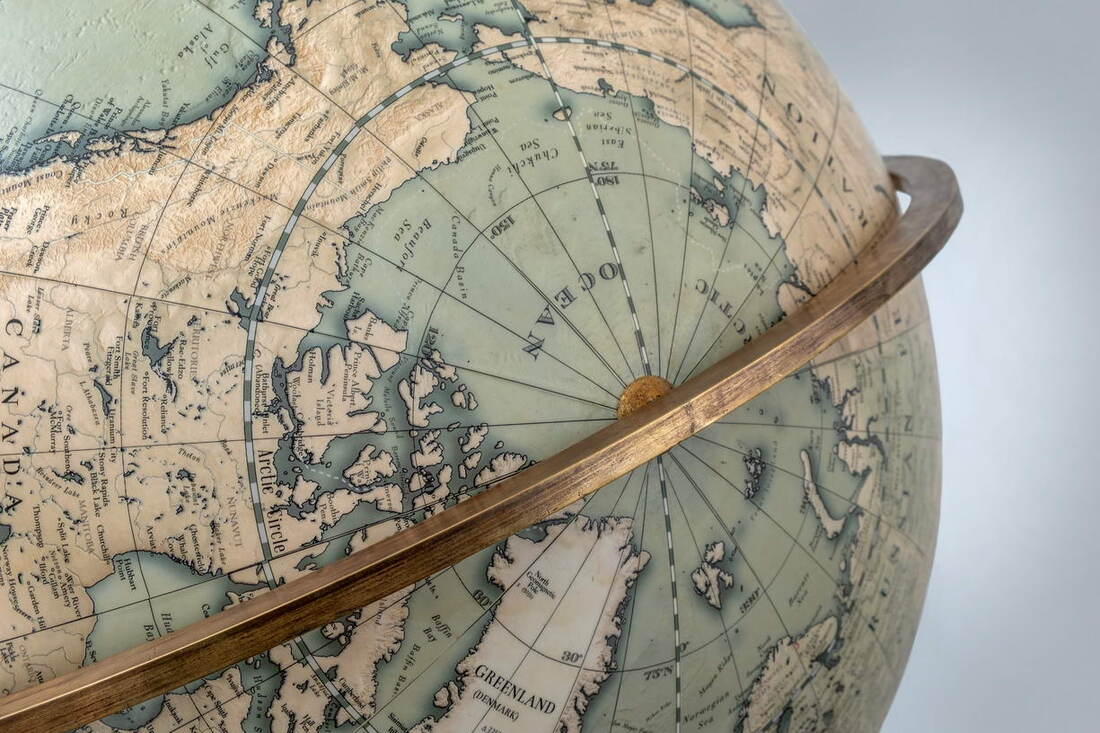 A globe that can be spun 360 degrees showing the North Pole. It has an aged brass arm and the green globe looks antique.